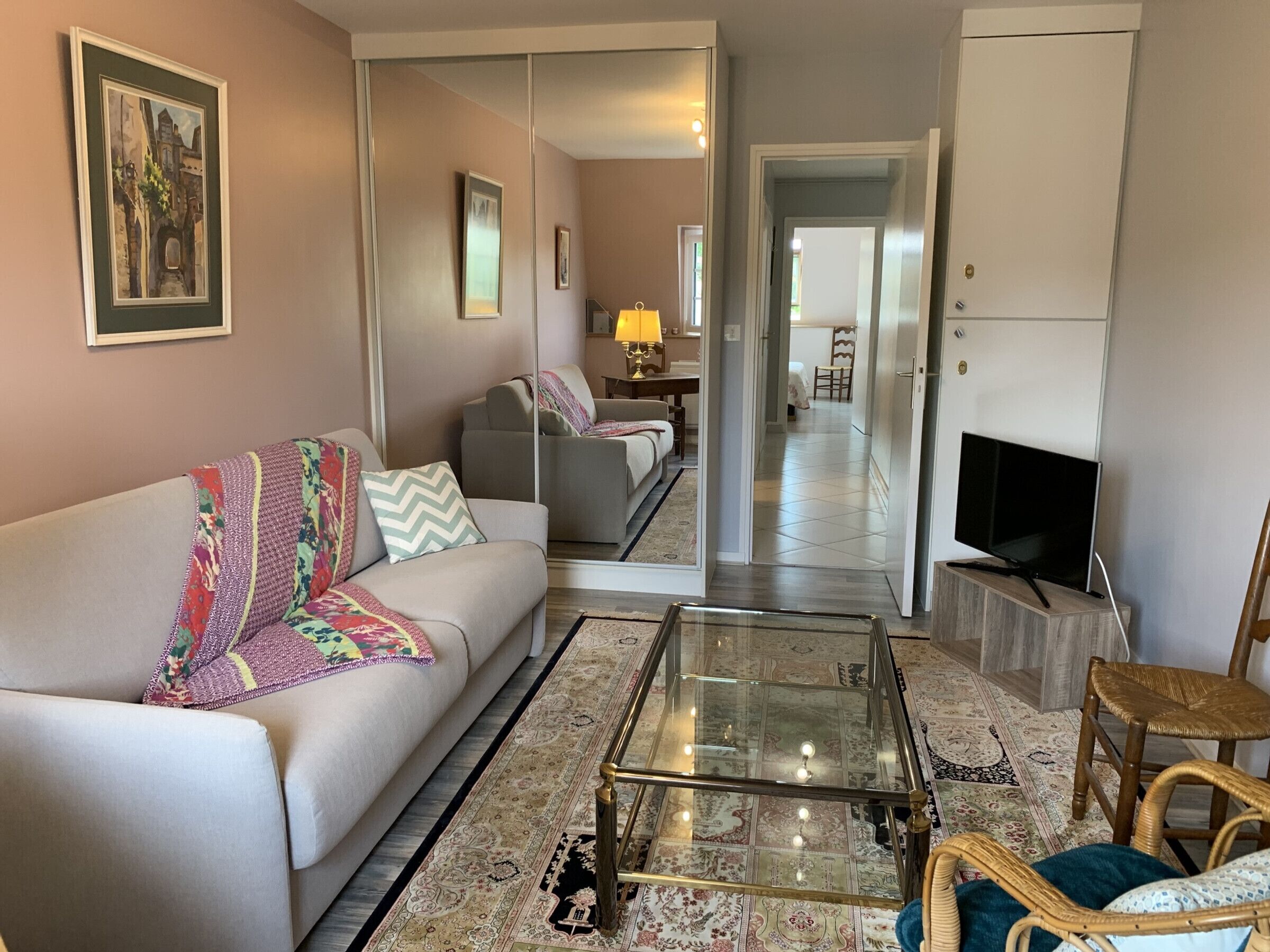 A living room with a sofa, a glass coffee table, a TV, and a mirror reflecting the room.