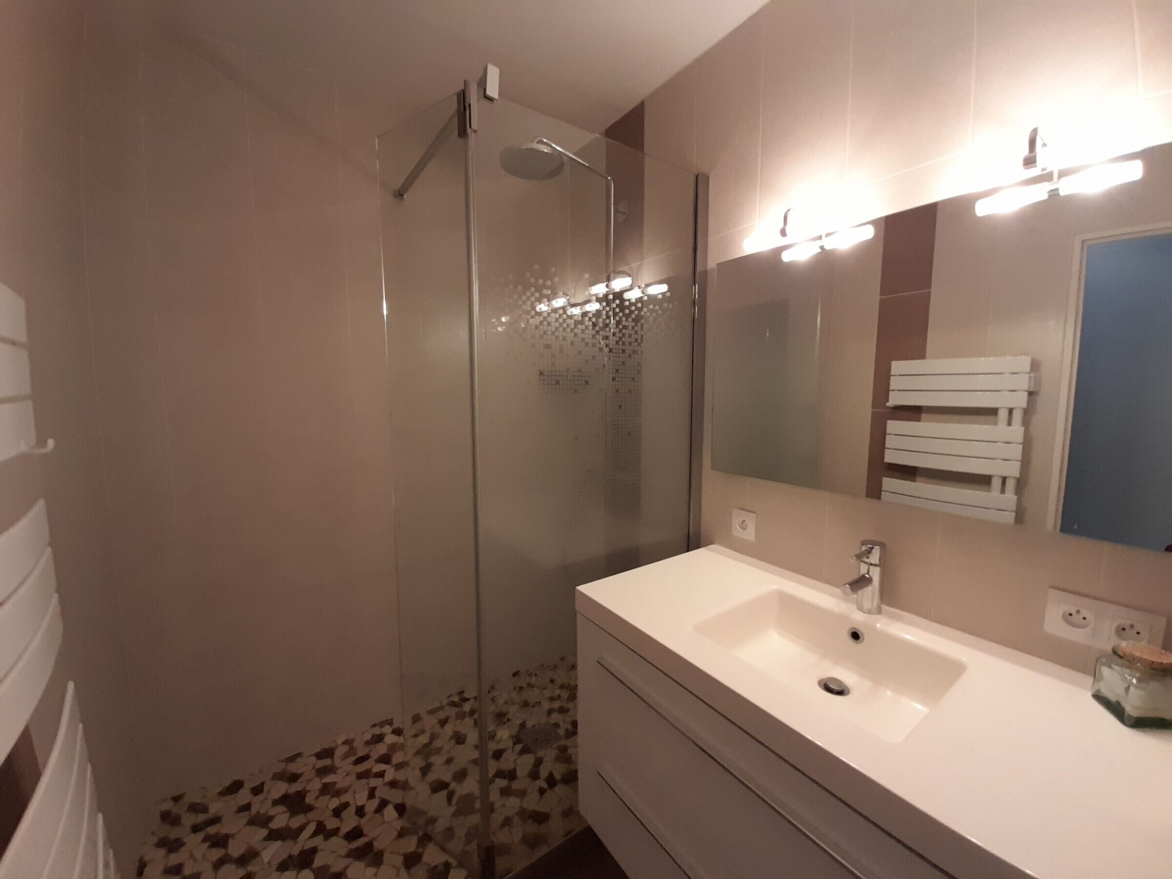 A bathroom with a glass-enclosed shower, a white sink, and a mirror with lights.