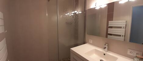 A bathroom with a glass-enclosed shower, a white sink, and a mirror with lights.