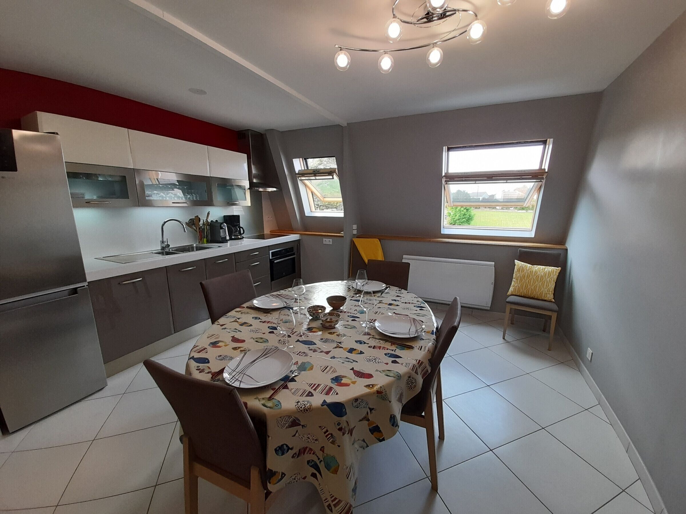 Una cocina moderna con comedor, que incluye una mesa redonda preparada para cuatro personas, un horno empotrado y un ventanal que proporciona luz natural.