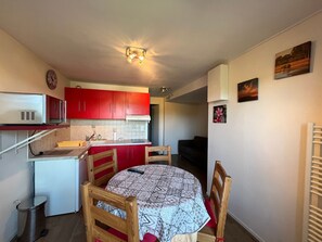 A compact kitchen with red cabinets, a microwave, and a dining area with a patterned tablecloth.