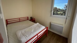 A bedroom with a single bed, a nightstand, a window with a view, and a radiator. - T2 with terrace and Wi-Fi, near Thermes du Connétable (La Roche-Posay)