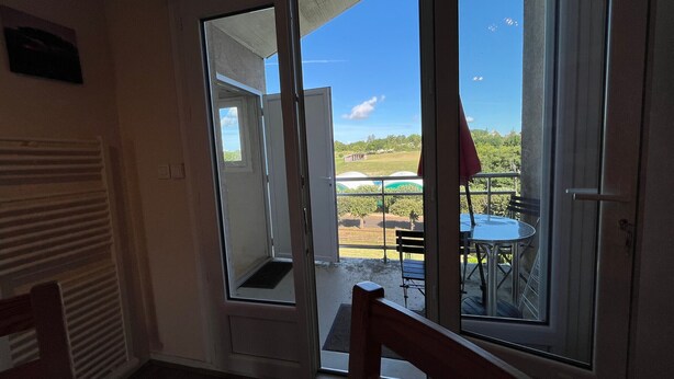 An open door leading to an outdoor patio with a table and chairs, a view of the sky, and a building in the distance. - T2 with terrace and Wi-Fi, near Thermes du Connétable (La Roche-Posay)