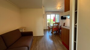 A compact living space with a sofa, a dining table with chairs, a kitchen area with cabinets, and a sliding glass door leading to an outdoor area. - T2 with terrace and Wi-Fi, near Thermes du Connétable (La Roche-Posay)