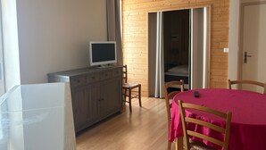 A room with a wooden floor, a dining table with chairs, a TV on a cabinet, and a sliding door leading to a bedroom. - Cozy 70m² apartment with WIFI near Saint Roch hot springs (La Roche-Posay)