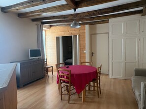 A dining area with a wooden table and chairs, a television on a cabinet, and a door leading to another room.