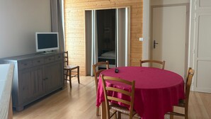 A room with a wooden dining table, chairs, a TV on a cabinet, and a door leading to another room. - Cozy 70m² apartment with WIFI near Saint Roch hot springs (La Roche-Posay)