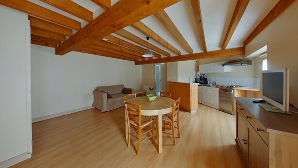 A spacious loft with a high ceiling, exposed wooden beams, a dining area with a round table and chairs, a kitchenette, and a sofa. - Cozy 70m² apartment with WIFI near Saint Roch hot springs (La Roche-Posay)