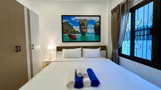 A hotel room with a bed, a painting of a boat on water, a nightstand, and a window with curtains. - Bayok 10 - 2 Bedroom Villa Near Kathu Waterfall (Kathu)