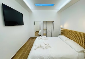 A modern hotel room with a large bed, a flat-screen TV mounted on the wall, a skylight, and a wooden headboard. - Prestigious Villa Olimpo With Pool And Sea View (Avola)