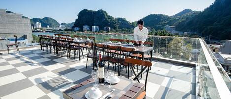 Terraza en la azotea con mesas dispuestas para comer, con vistas panorámicas a montañas y un cuerpo de agua.