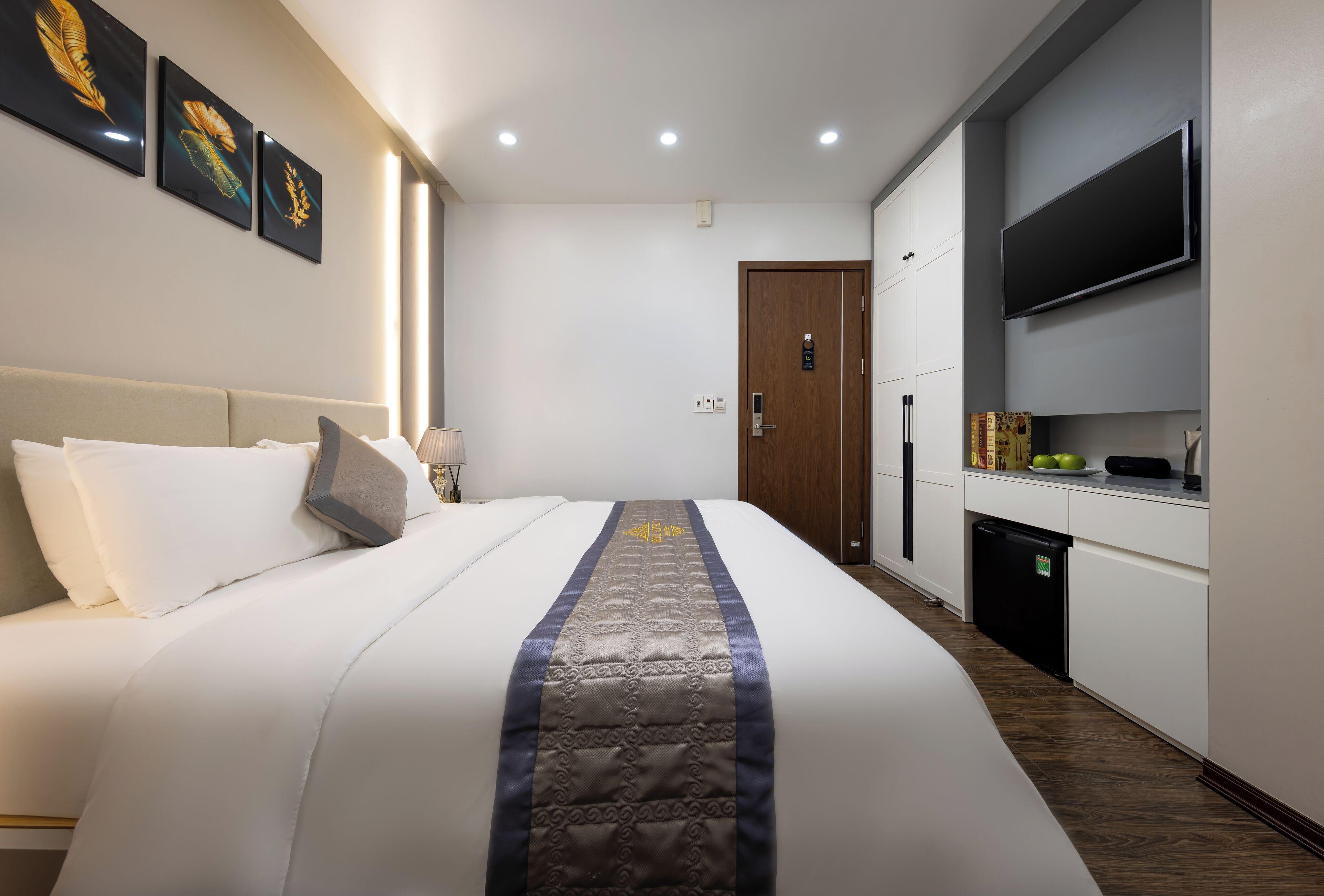 Een hotelkamer met een groot bed, een televisie, een minibar en een deur naar de badkamer.