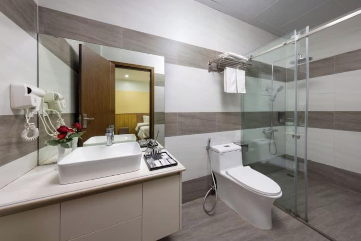 Un baño moderno con un espejo grande, un lavamanos blanco, un inodoro y una zona de ducha con mampara de vidrio.