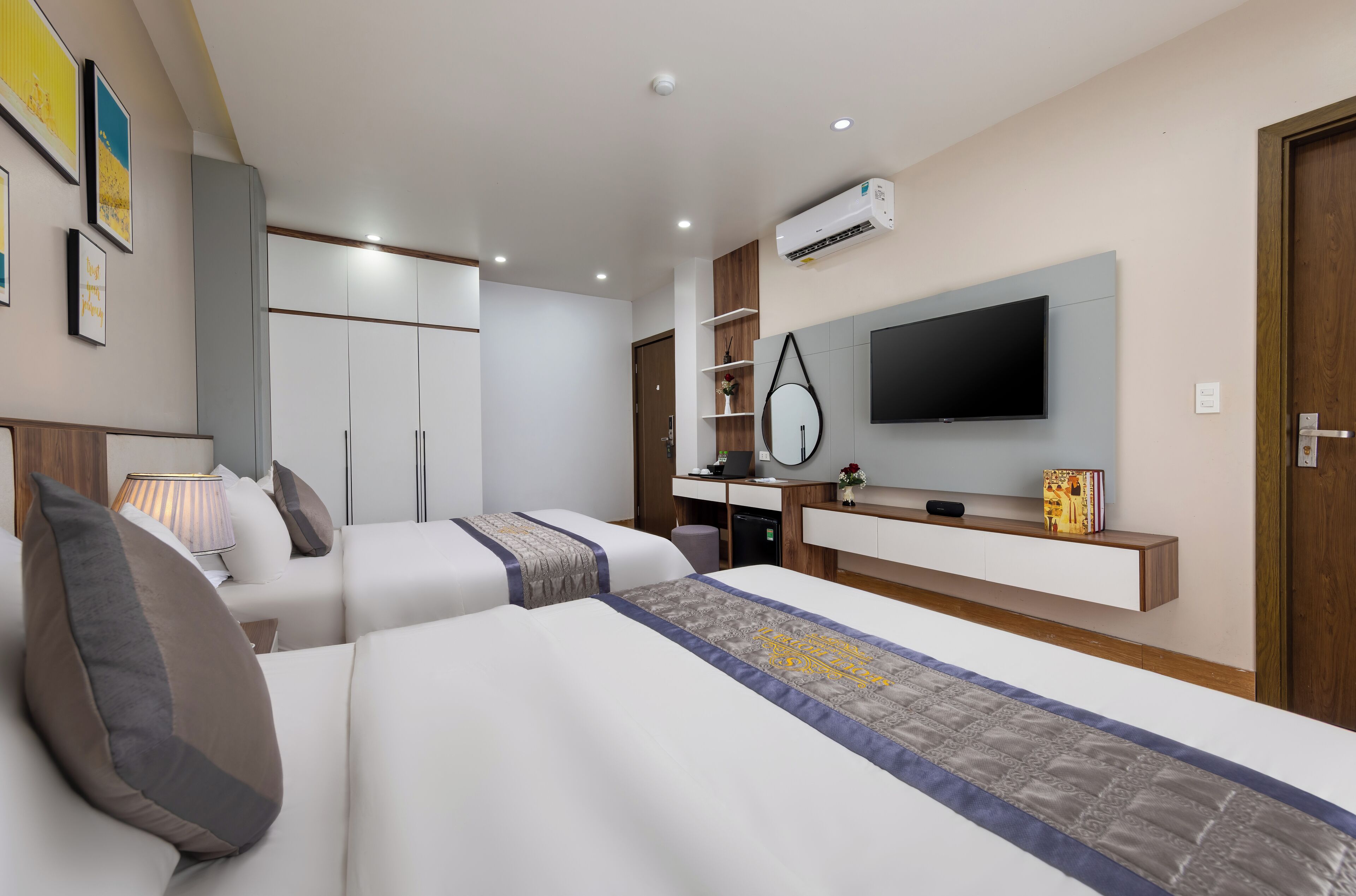 Ein modernes Hotelzimmer mit zwei Betten, einem Fernseher, einem Schreibtisch und einem Kleiderschrank.