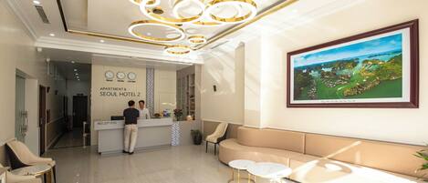 A hotel reception area with a modern design, including a reception desk, seating area, and a large framed landscape painting on the wall.
