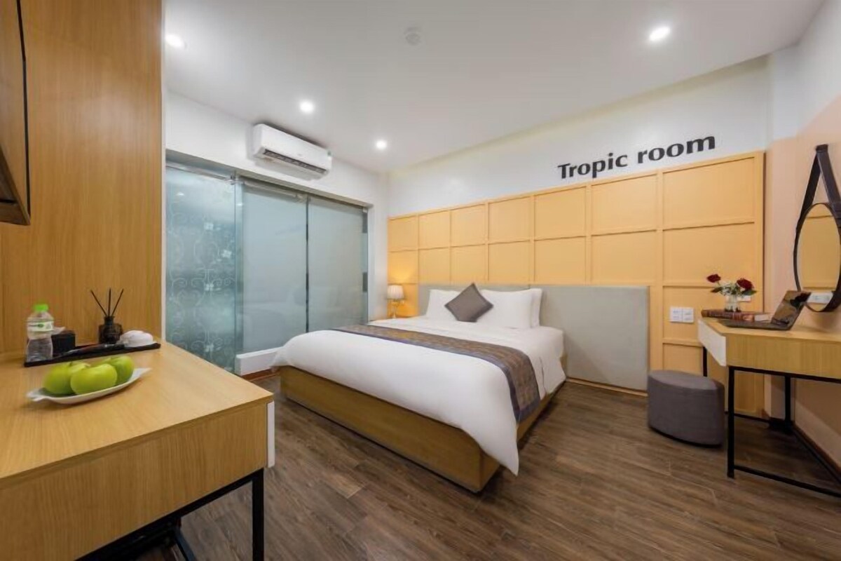 A hotel room with a bed, a desk, a mirror, and a 'Tropic room' sign.