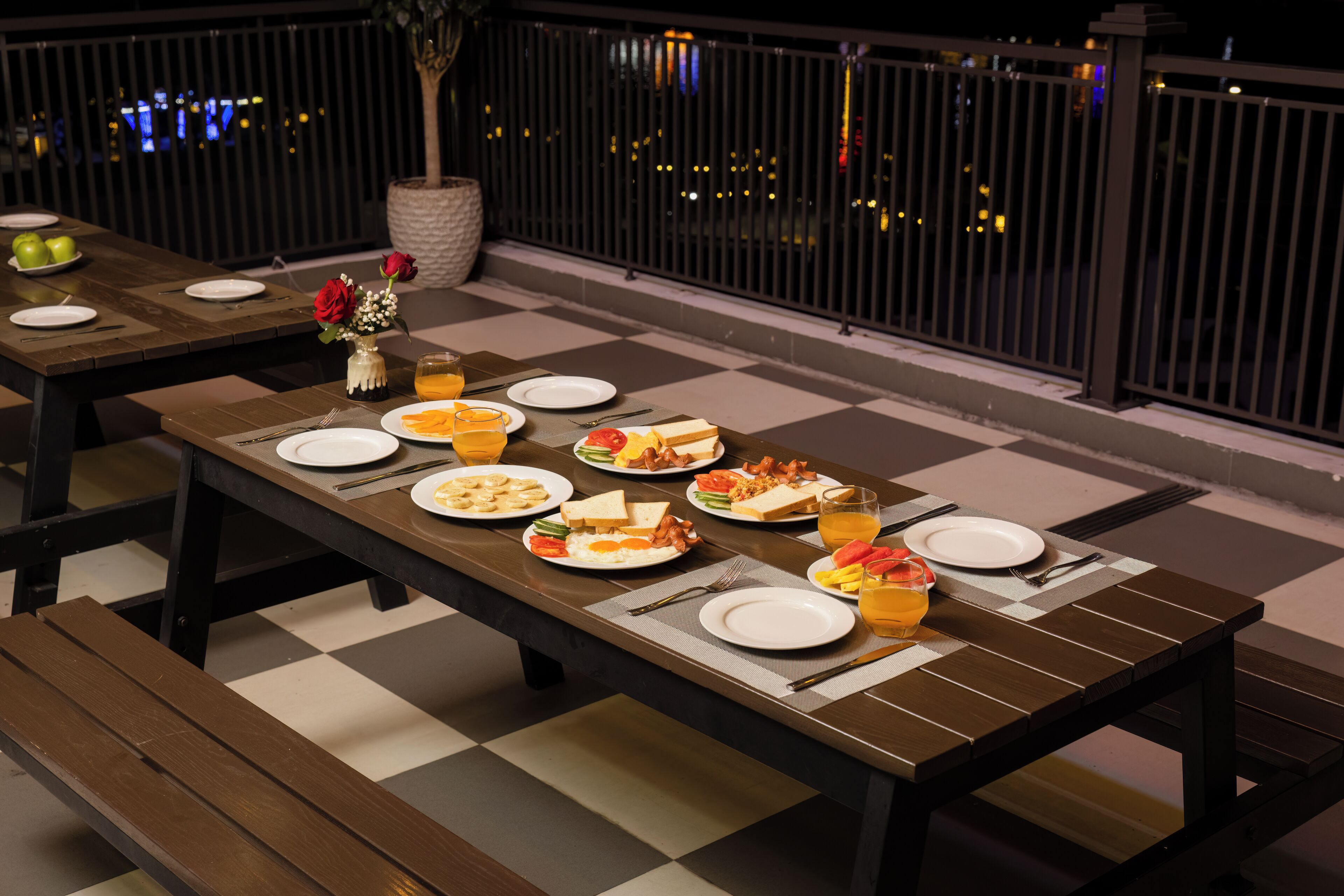 A dining area with tables set for meals, a view of the city at night, and a railing.
