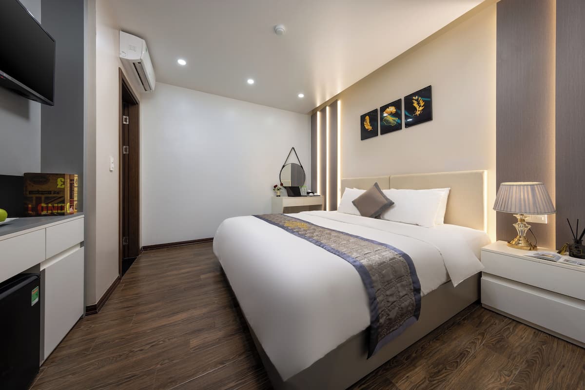 A modern hotel room with a large bed, bedside tables, a TV, and an air conditioning unit.