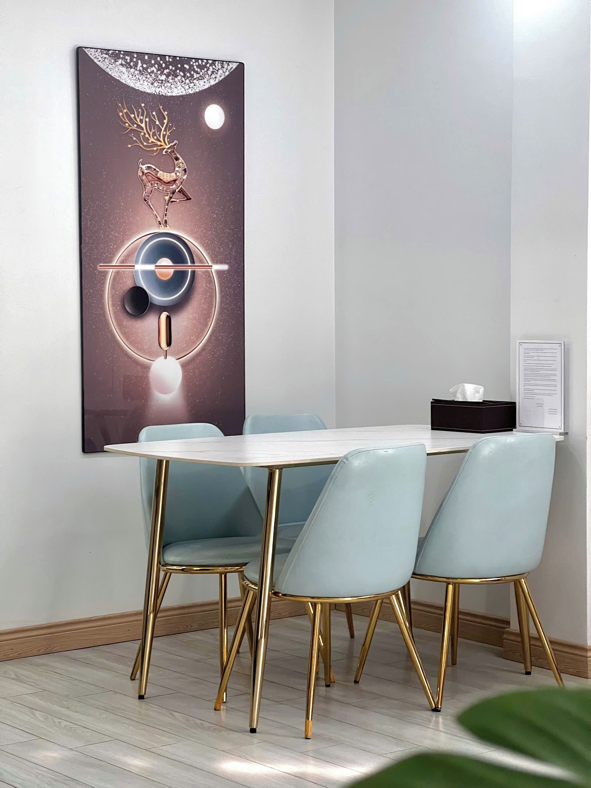 A dining area with a round table, four light blue chairs with gold legs, and a modern abstract painting on the wall.