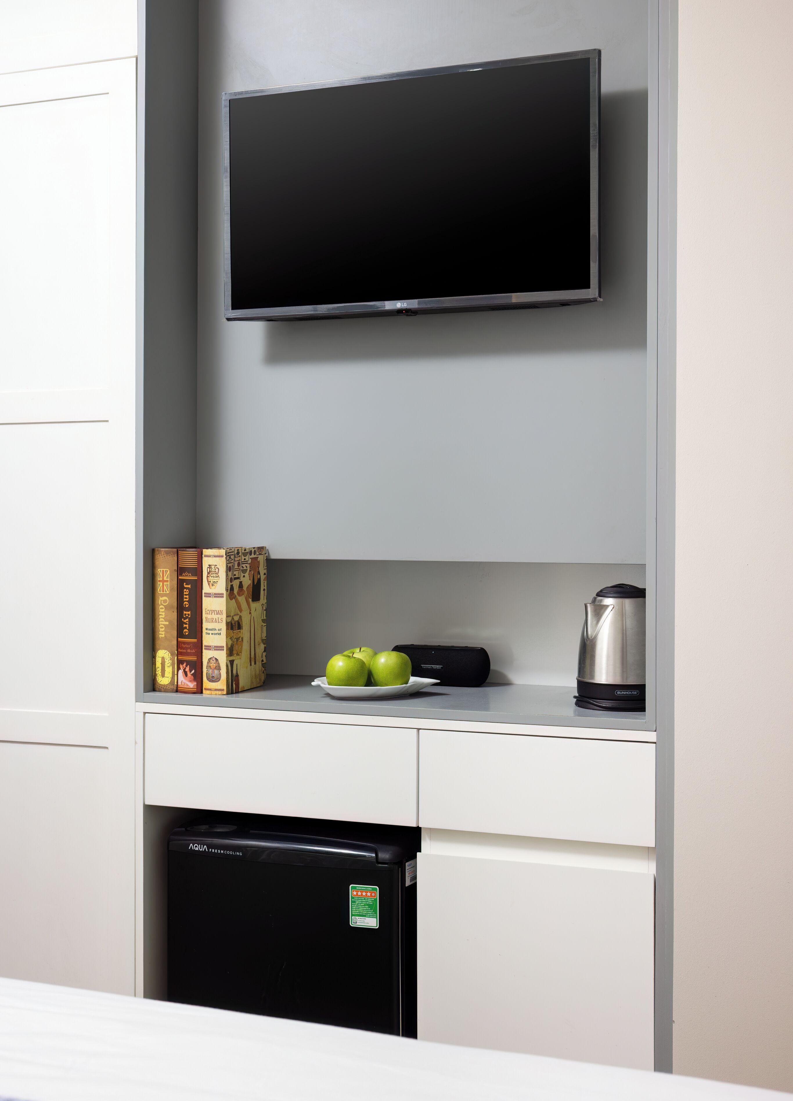 A kitchen with a flat-screen TV mounted above a countertop, a dishwasher below, and a kettle on the counter.