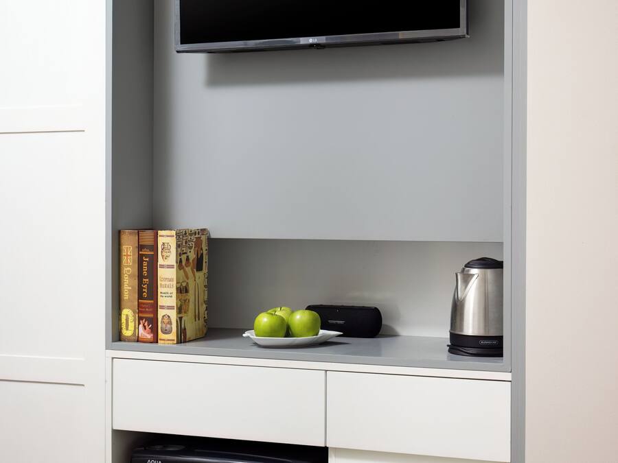 A kitchen with a flat-screen TV mounted above a countertop, a dishwasher below, and a kettle on the counter.