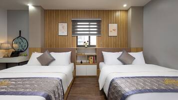 Habitación de hotel con dos camas, un escritorio pequeño, una ventana con persianas y un estante en la pared con libros y un florero.