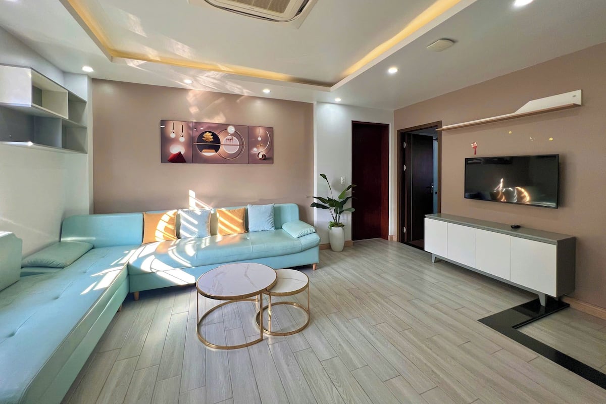 A modern living room with a sectional sofa, a coffee table, a flat-screen TV, and a decorative wall piece.