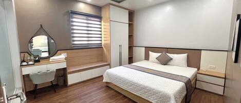 A modern bedroom with a large bed, a bedside table, a wardrobe, a vanity with a mirror, and a bench.