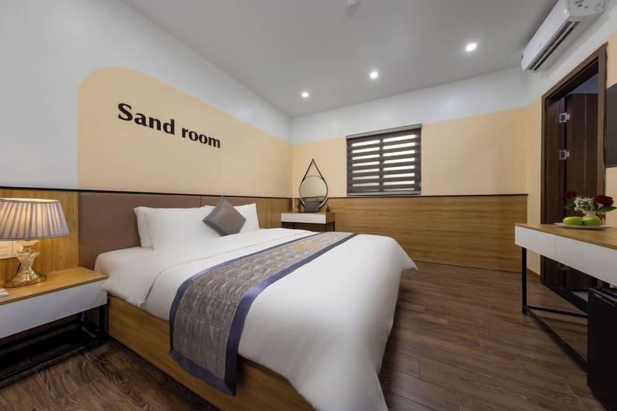 A hotel room with a bed, bedside table, lamp, and a wall sign reading "Sand room".