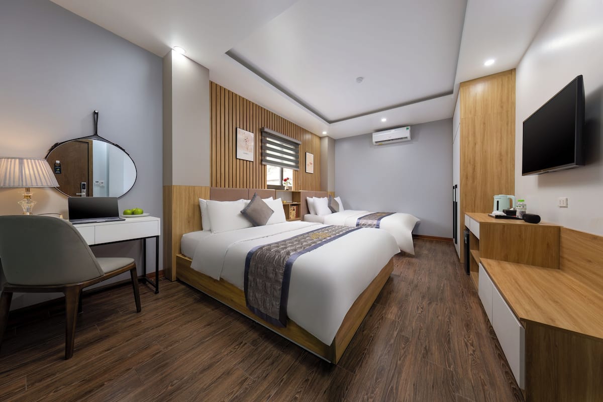A modern hotel room with a large bed, a desk with a laptop, a chair, and a TV mounted on the wall.