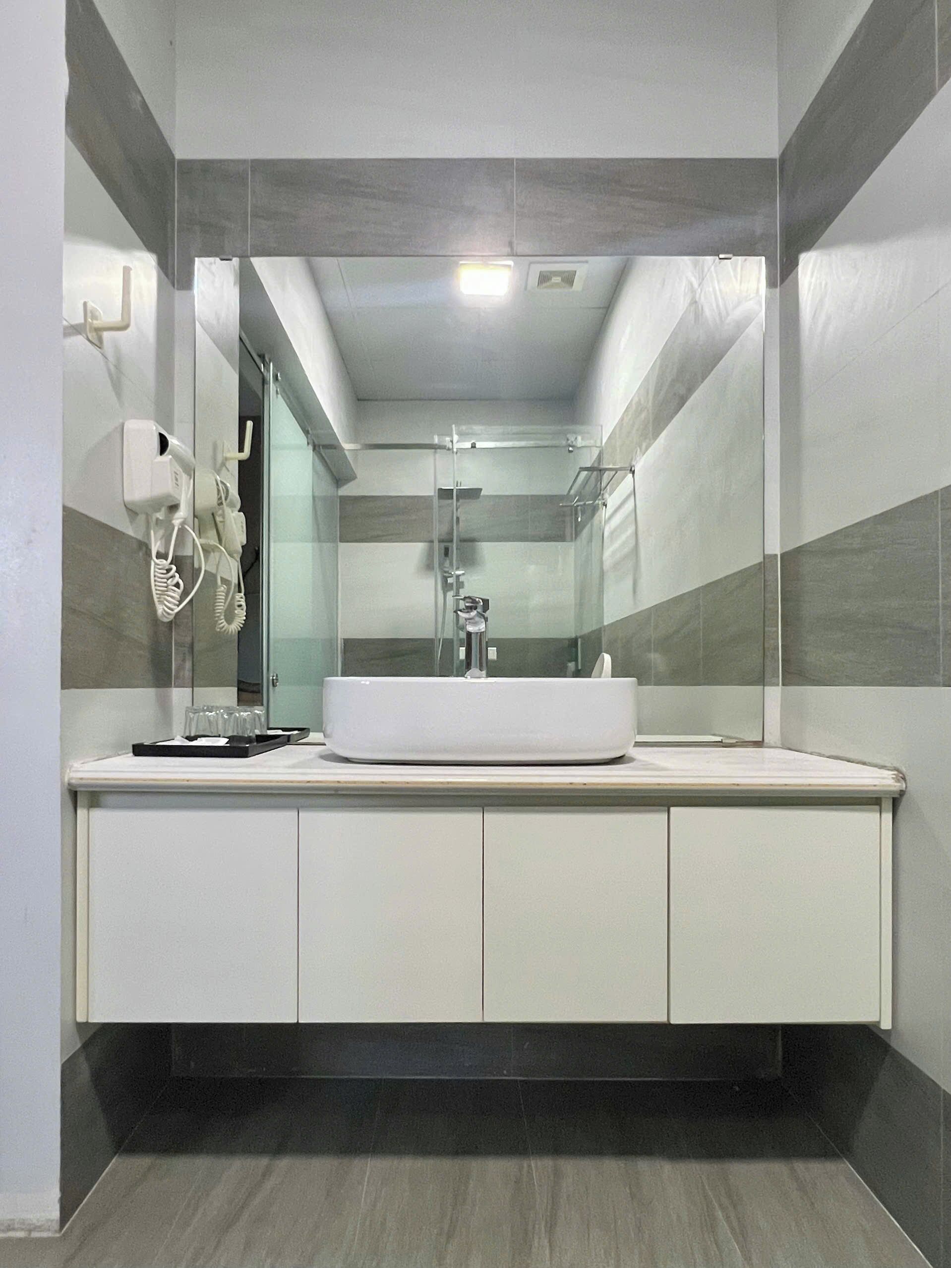 A modern bathroom with a large mirror, a white sink, and a glass shower enclosure.