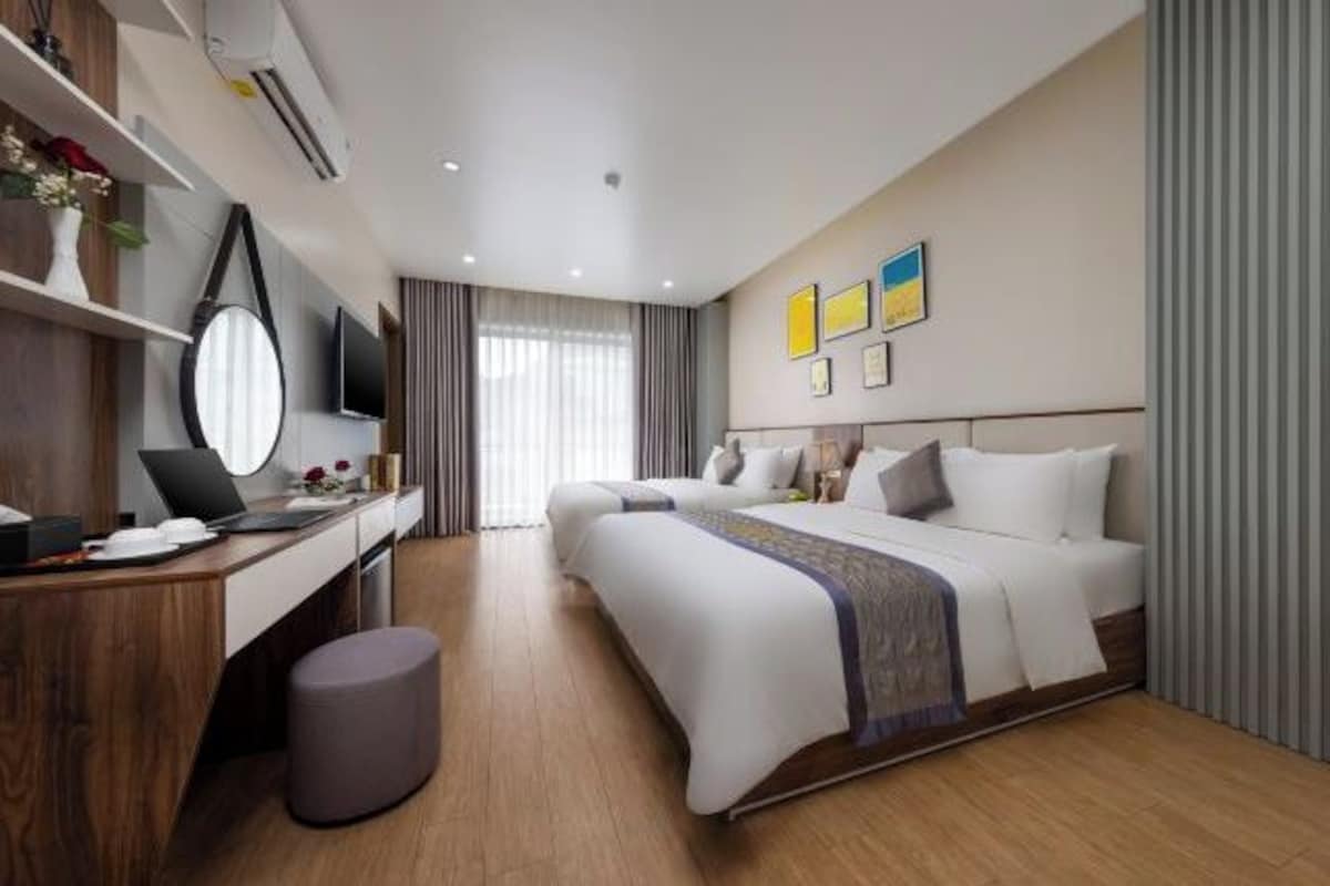 Una habitación de hotel moderna con un escritorio de madera, una cama con ropa blanca, un taburete gris y un televisor de pantalla plana.