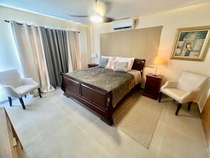 A bedroom with a large bed, two bedside tables, a ceiling fan, and a painting on the wall.