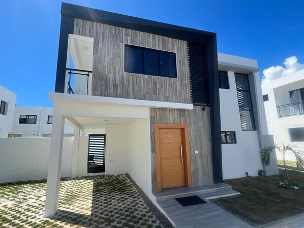 A modern two-story house with a wooden door, a balcony, and a small garden area.