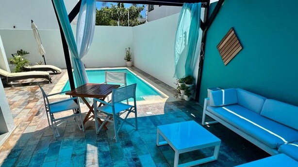 A poolside area with a table and chairs, a sofa, and a small table. - Sky I Village Bavaro (Punta Cana)