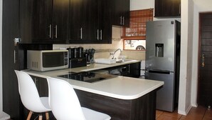 Una cocina moderna con armarios oscuros, un refrigerador de acero inoxidable, un microondas y una encimera blanca.