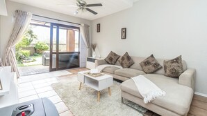 Una sala de estar con un sofá, una mesa de centro y un ventilador de techo. Hay una puerta corrediza de vidrio que da a un patio.