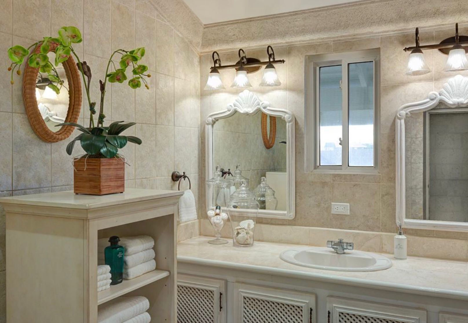 A bathroom with a large mirror, two wall-mounted lights, a sink, and a shelf with towels and a potted plant.