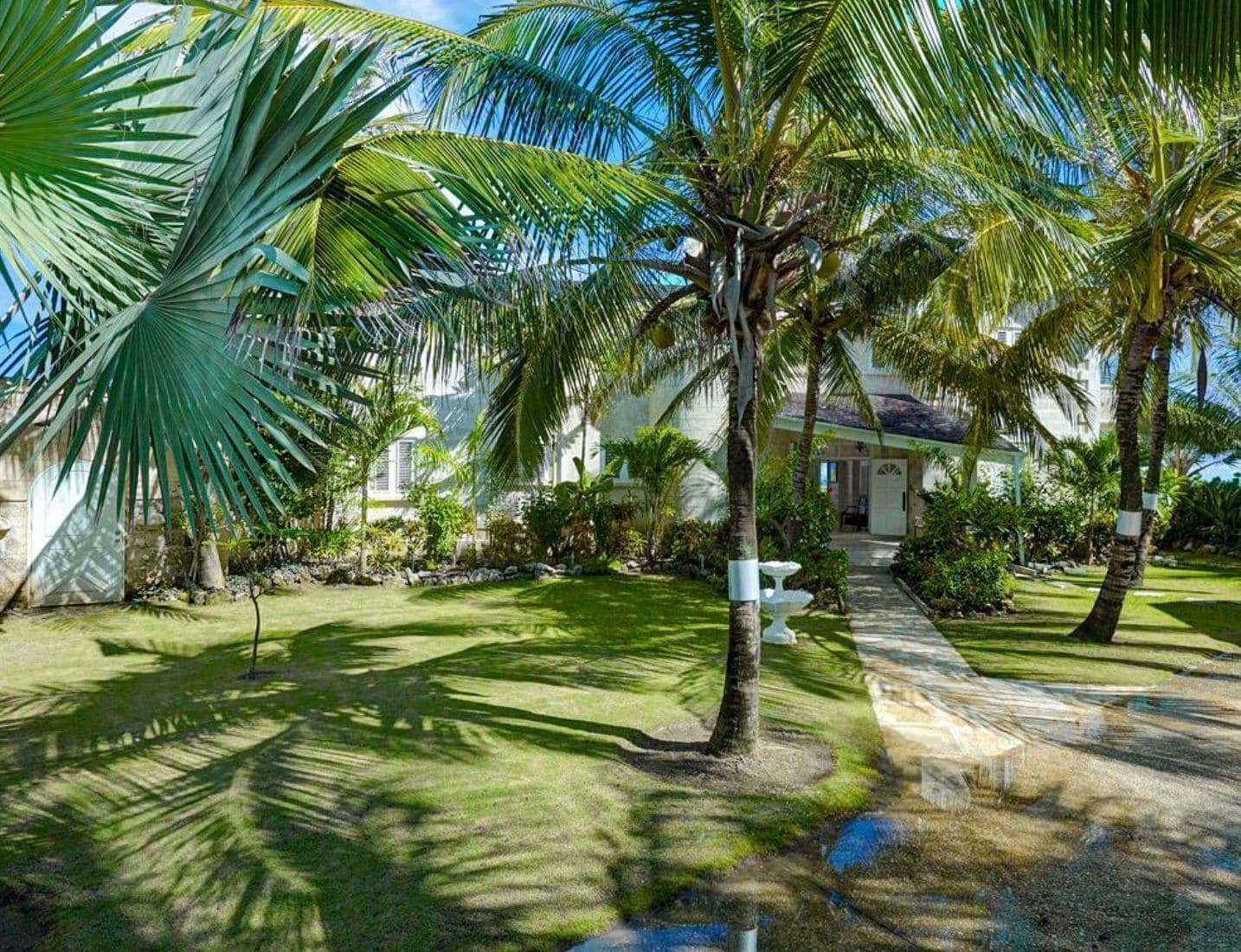 Un resort tropical con palmeras, un césped cuidado y un sendero que lleva a un edificio.