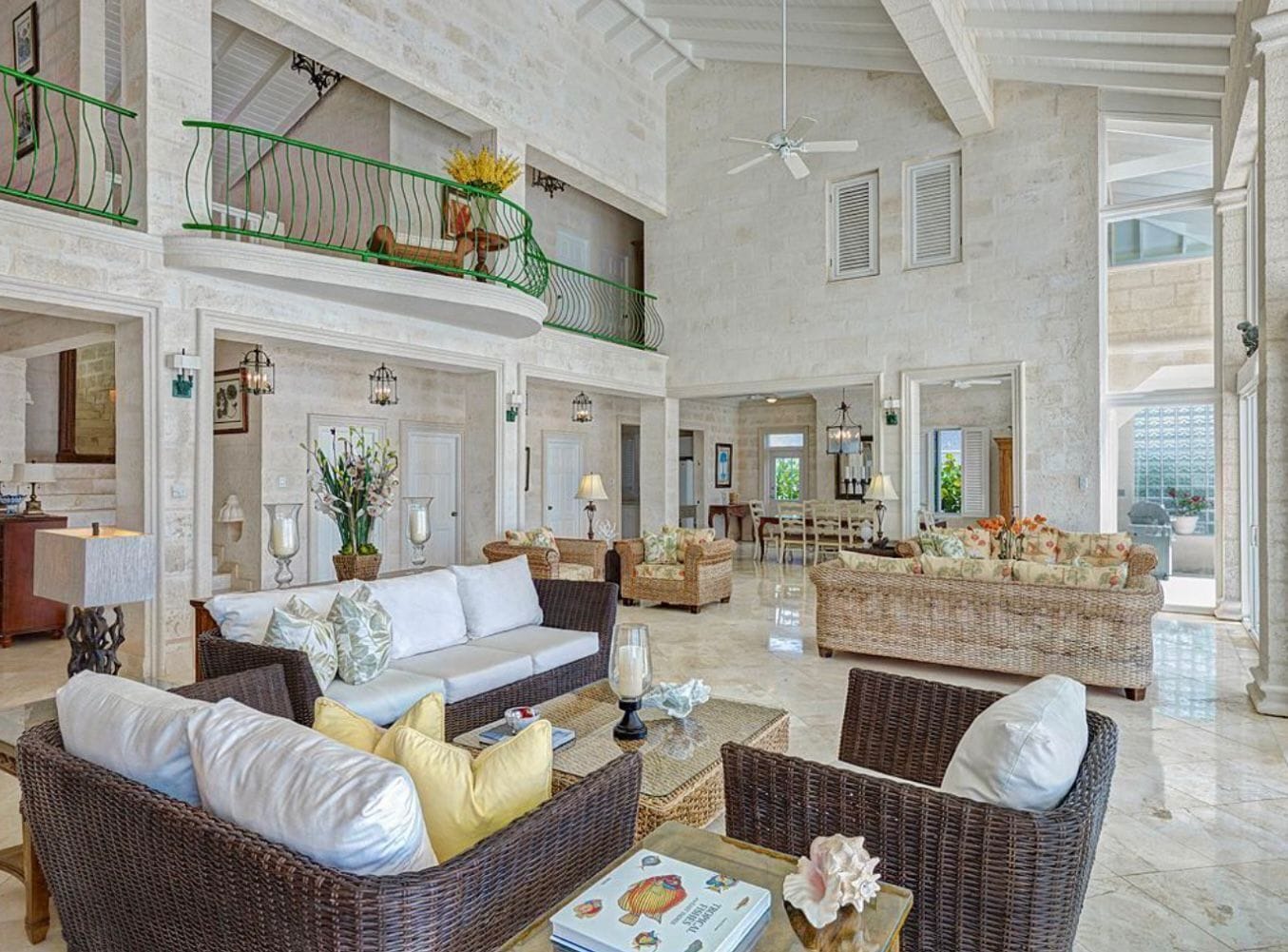 A spacious living area with wicker furniture, a balcony with a green railing, and a ceiling fan.
