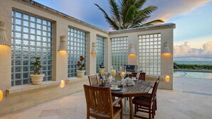 Uma sala de jantar com uma mesa posta para seis pessoas, rodeada por janelas amplas com painéis de vidro decorativos.