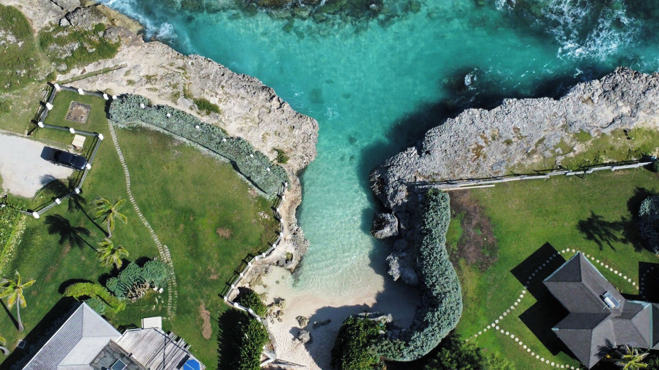 Vista aérea de una propiedad costera con playa, un pequeño muelle y un camino pavimentado.