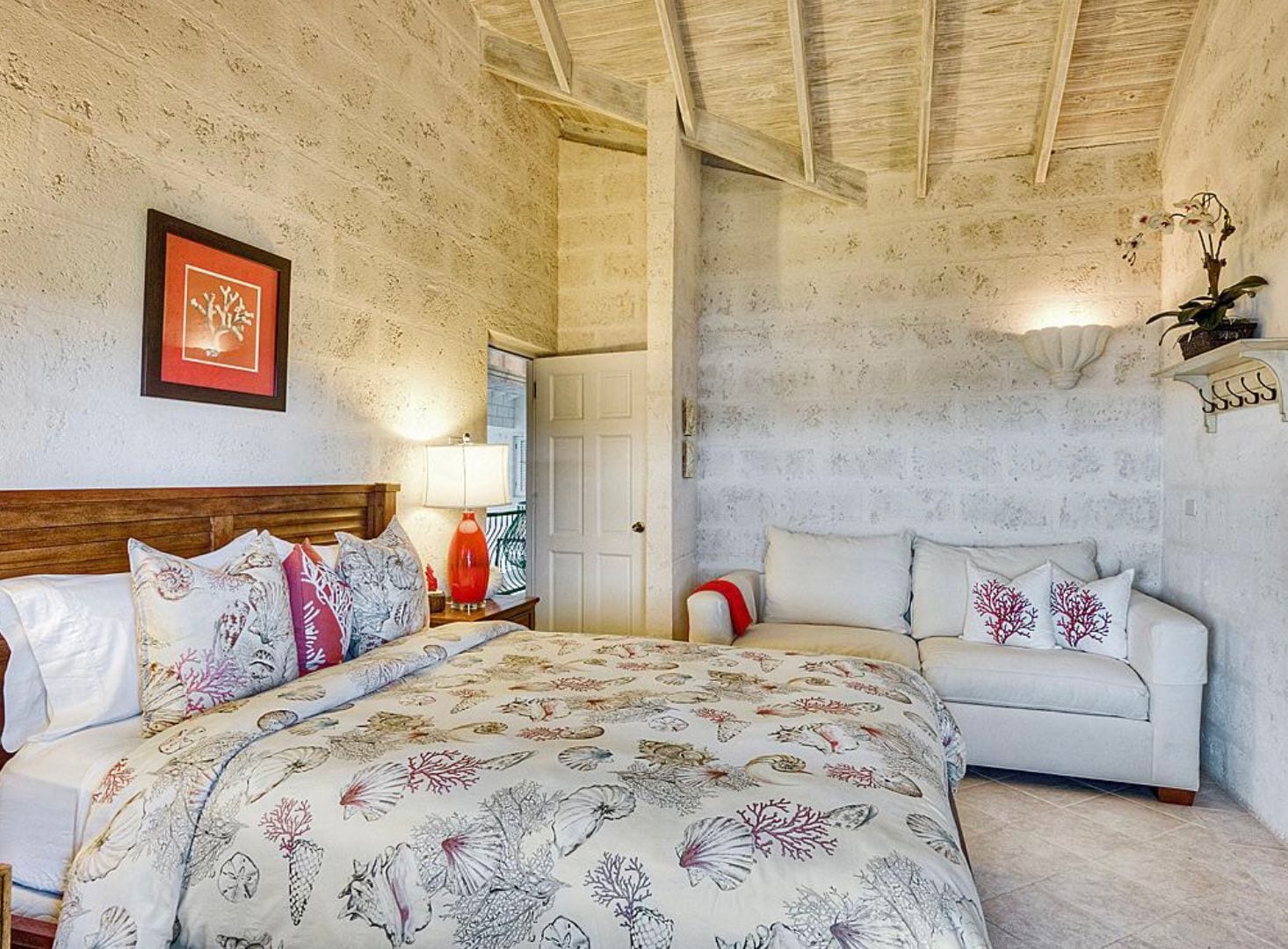 A bedroom with a bed, a nightstand, a lamp, a sofa, and a framed picture on the wall.