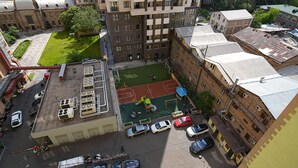 A multi-story building with a basketball court, parking area, and several cars parked in front. - Mount Ararat View 2-bedroom Luxury Apartment by Sweet Home (Yerevan)