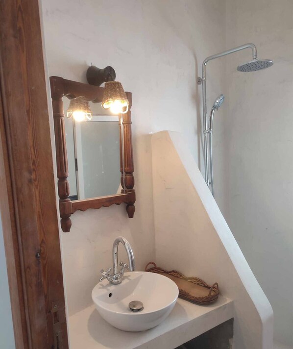 Un baño con lavamanos blanco, espejo con marco de madera y ducha.