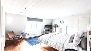 Une chambre à coucher avec un lit, une chaise, une petite table, un téléviseur et un ventilateur.