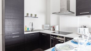 Une cuisine moderne avec des meubles de couleur sombre, un plan de travail blanc, un four encastré et un four à micro-ondes.
