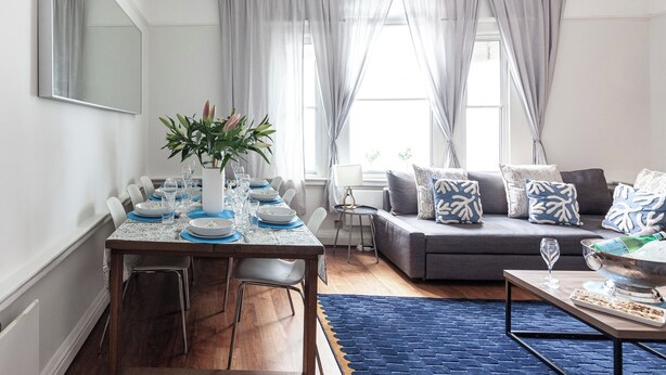 Un salon moderne comprenant un coin repas, un ensemble de canapés gris et un tapis bleu.