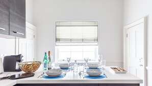 Une cuisine moderne avec des meubles blancs, un îlot central agrémenté de sets de table bleus et une fenêtre avec des stores.