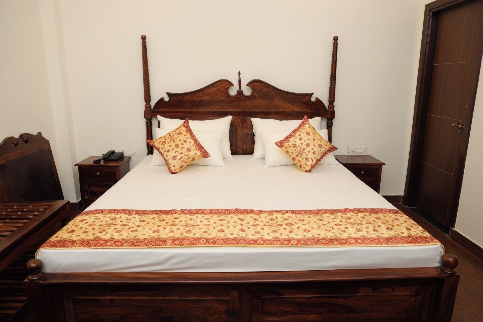 Un letto rifatto con cura, con una testiera in legno, due comodini con lampade e una coperta a motivi decorativi.